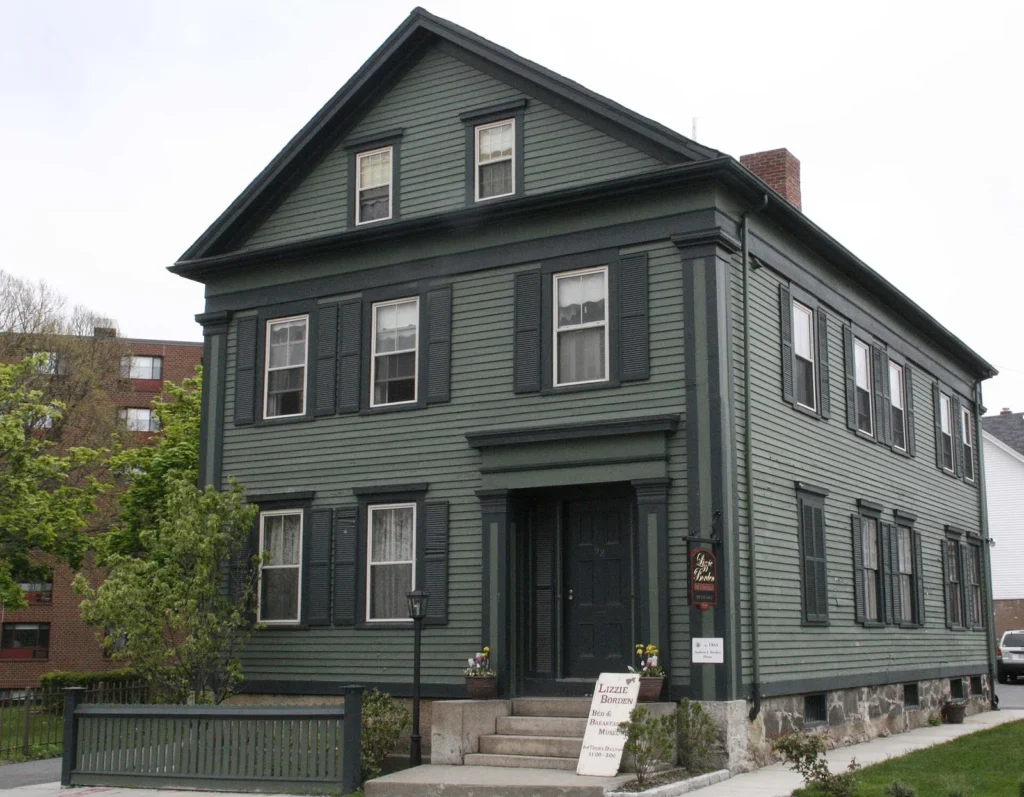Green two-story clapboard house with dark shutters, a front porch and a bed and breakfast sign on the steps, the Lizzie Borden House in Fall River, Massachusetts
