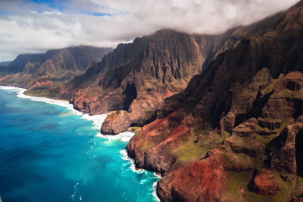 Aerial view of the Na Pali Coast on Kauai, with deeply fluted green cliffs dropping straight into turquoise ocean.