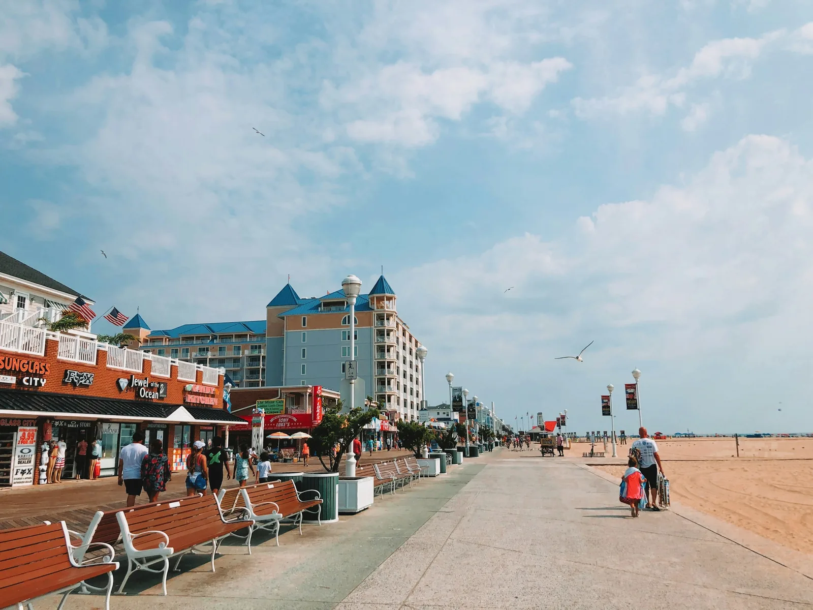 Pedestrians strolling along the wooden planks of the Ocean City boardwalk next to beachside buildings in Maryland