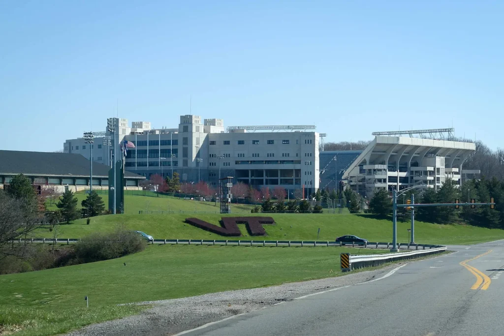 Exterior of Lane Stadium in Blacksburg, Virginia, with the VT logo trimmed into a grassy hillside in front of the stone press box and grandstand