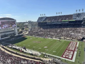 View from the upper deck of Davis Wade Stadium in Starkville, Mississippi, looking across the field toward a large videoboard and the packed east stands under a clear blue sky