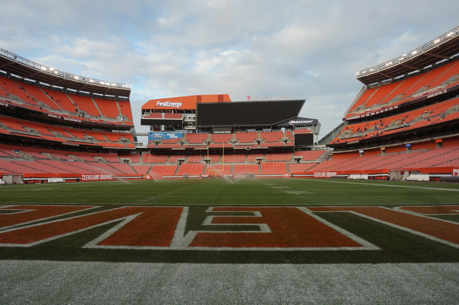 View from the sideline of the Cleveland Browns stadium before a game, with empty orange seats, the end zone lettering and the large video board, shown with its former FirstEnergy signage