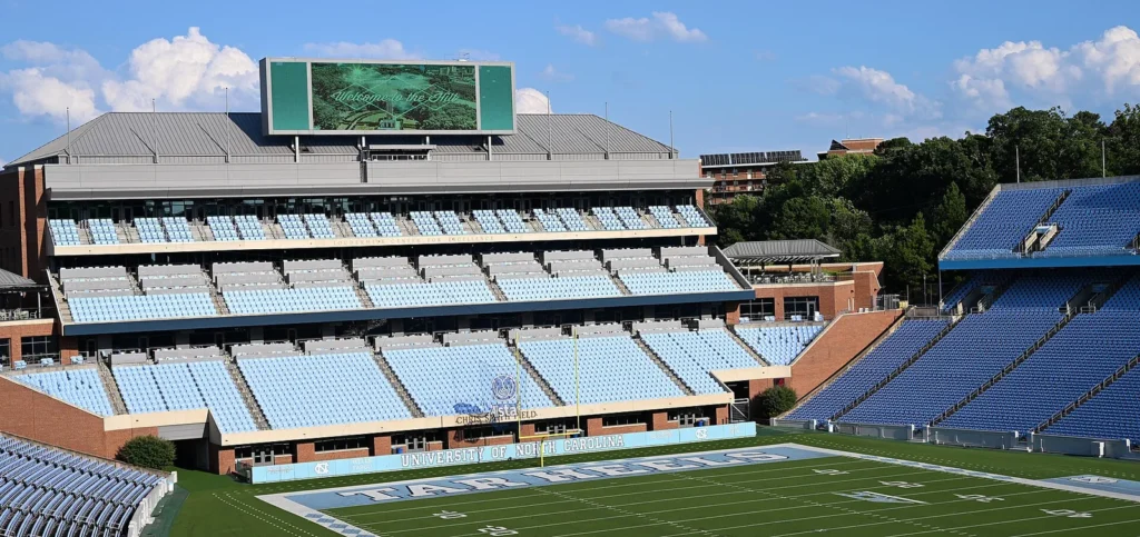 Empty light-blue and dark-blue seating at Kenan Stadium in Chapel Hill, with the videoboard above the press box and the Tar Heels end zone in the foreground
