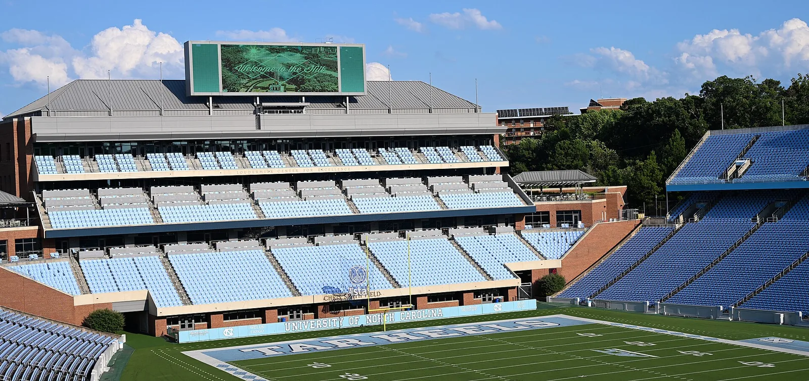 Empty light-blue and dark-blue seating at Kenan Stadium in Chapel Hill, with the videoboard above the press box and the Tar Heels end zone in the foreground